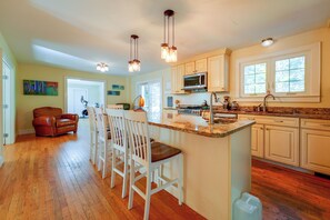 A kitchen with wooden flooring, white bar stools, a microwave, and a coffee maker. - Spacious Home w/ Fire Pit, 8 Mi to Dtwn Portland (Falmouth)