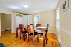 A dining room with a wooden table and chairs, a white cabinet, and a window with a view of trees. - Spacious Home w/ Fire Pit, 8 Mi to Dtwn Portland (Falmouth)