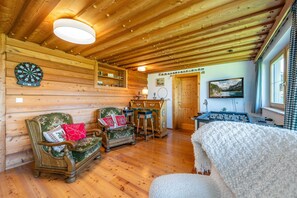 Quarto aconchegante com paredes de madeira, um alvo de dardo, um sofá, uma mesa com abajur e uma mesa de pebolim.