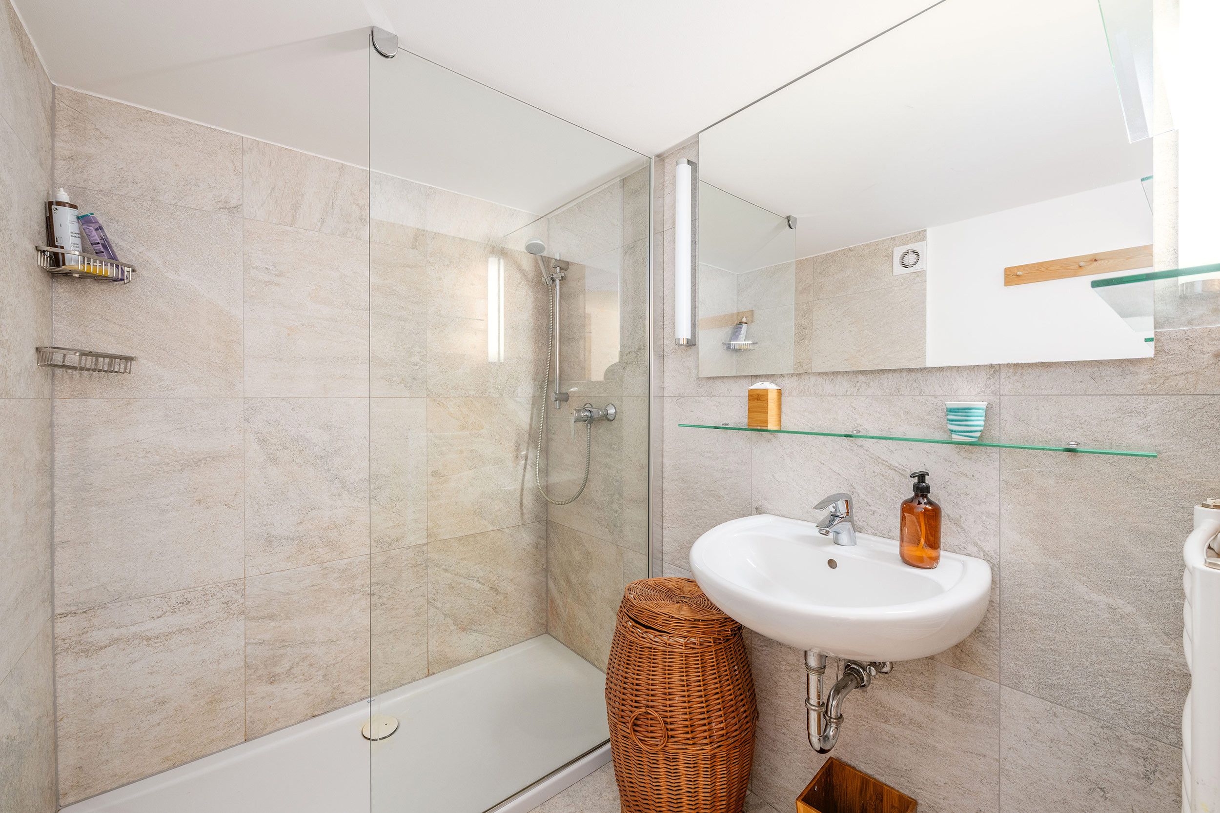 Ein modernes Badezimmer mit einer Duschkabine aus Glas, einer weißen Badewanne, einem weißen Waschbecken mit Seifenspender und einem Spiegel über dem Waschbecken.