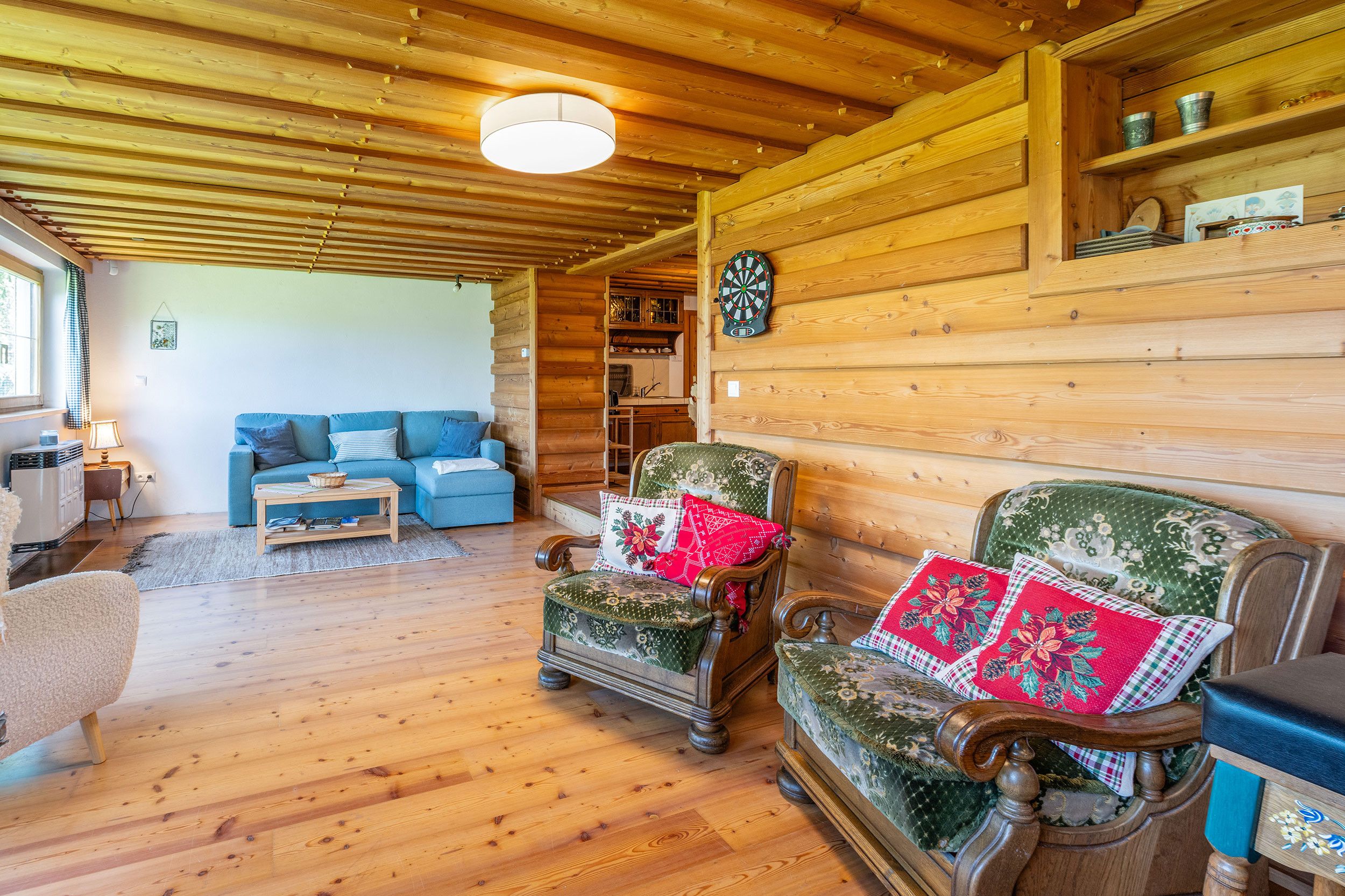 L’intérieur d’un chalet confortable, avec un plafond en bois, un canapé, un fauteuil recouvert d’un tissu à motifs floraux et un jeu de fléchettes.