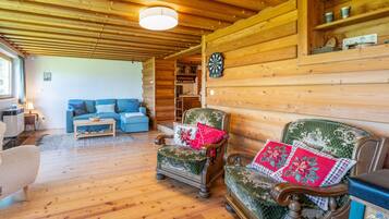 L’intérieur d’un chalet confortable, avec un plafond en bois, un canapé, un fauteuil recouvert d’un tissu à motifs floraux et un jeu de fléchettes.