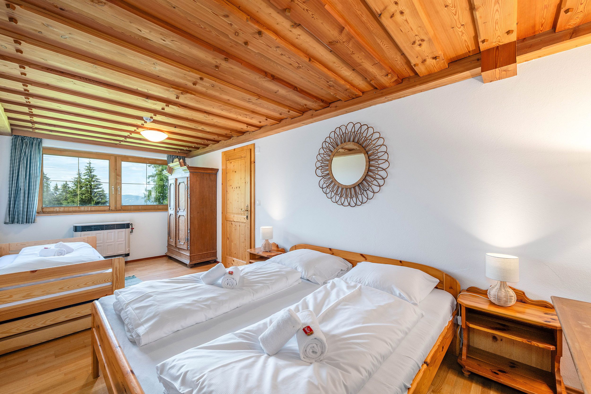 Ein Zimmer mit zwei Holzbetten, einem Spiegel und einem Fenster mit Blick auf Bäume.