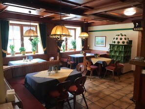 Un restaurant amb seients, taules, plantes en testos i una paret decorativa verda.