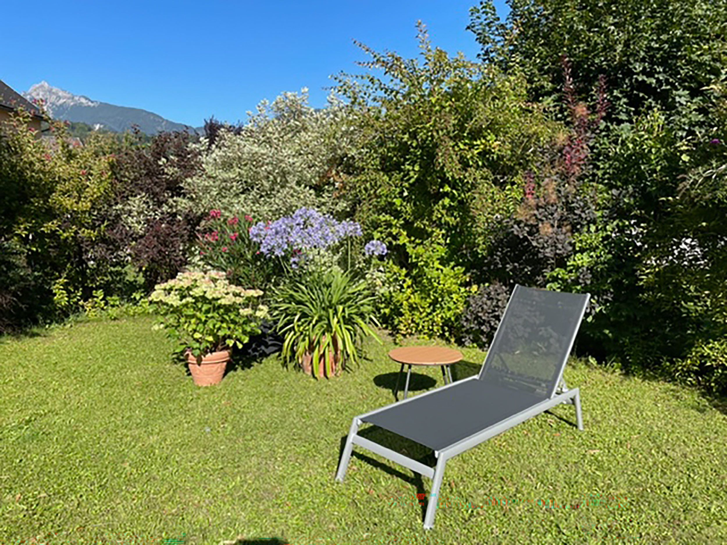 Ein Garten mit einem Metallstuhl, Topfpflanzen und einem kleinen Tisch.