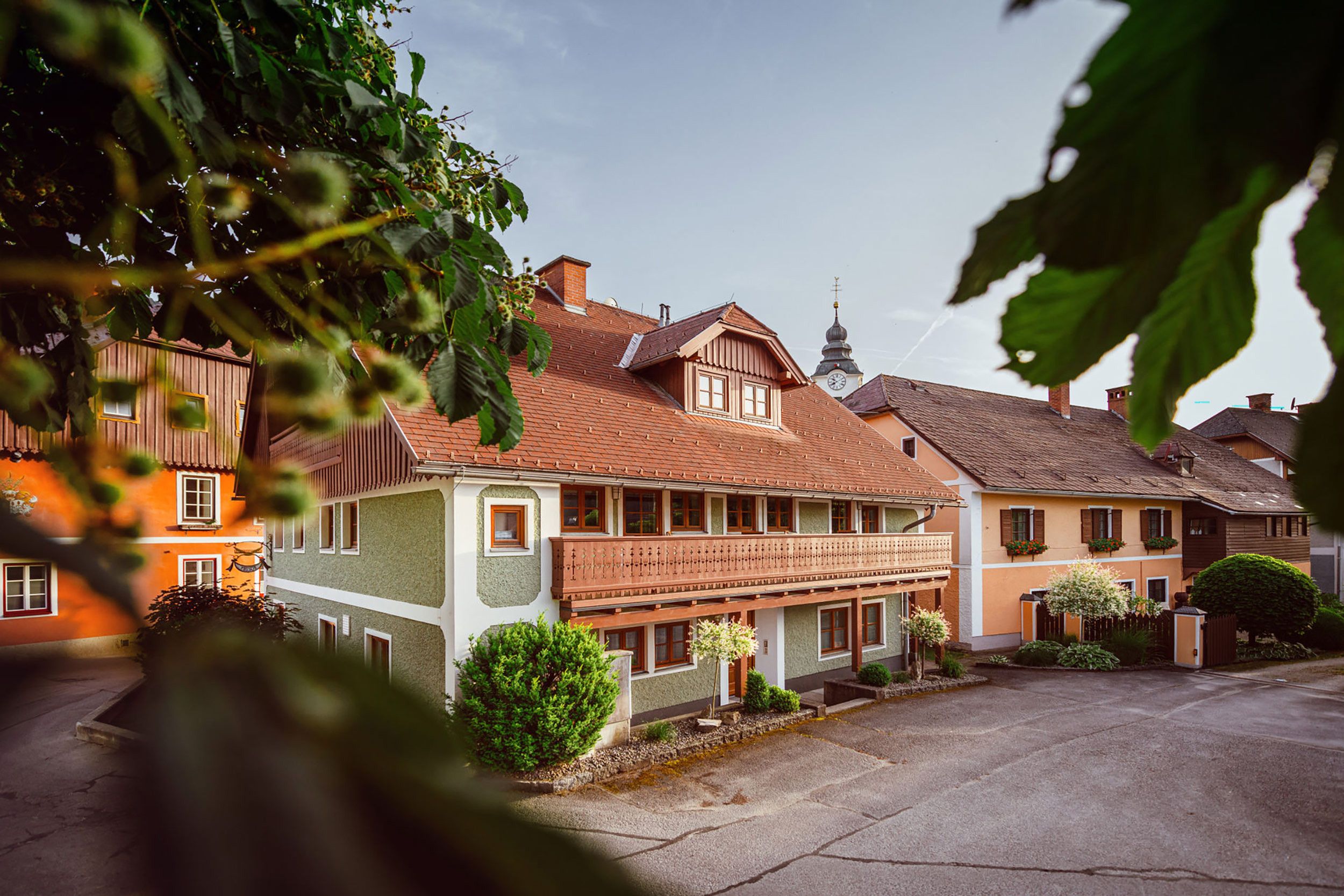 Un edificio de estilo europeo tradicional con un balcón, una torre del reloj al fondo y un patio empedrado.