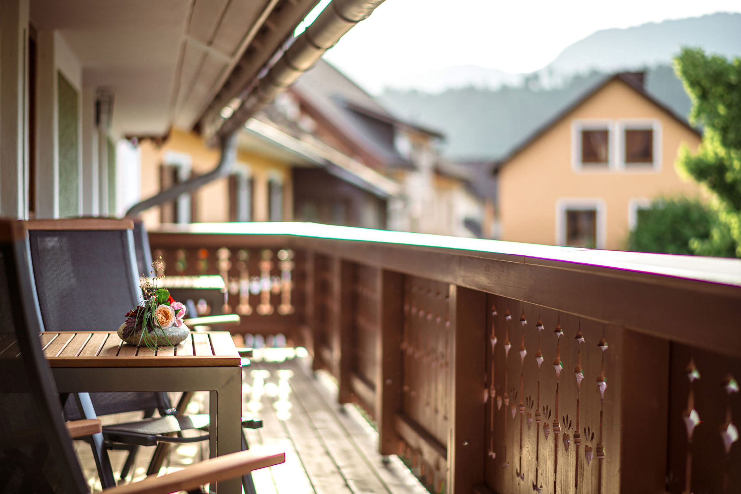 A wooden deck with a table and chairs, overlooking a row of houses with a mountain in the background.
