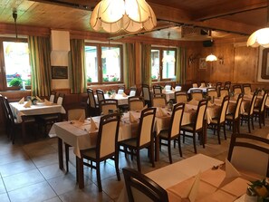 Un restaurant amb diverses taules i caires, grans finestres amb cortines i parets de fusta.