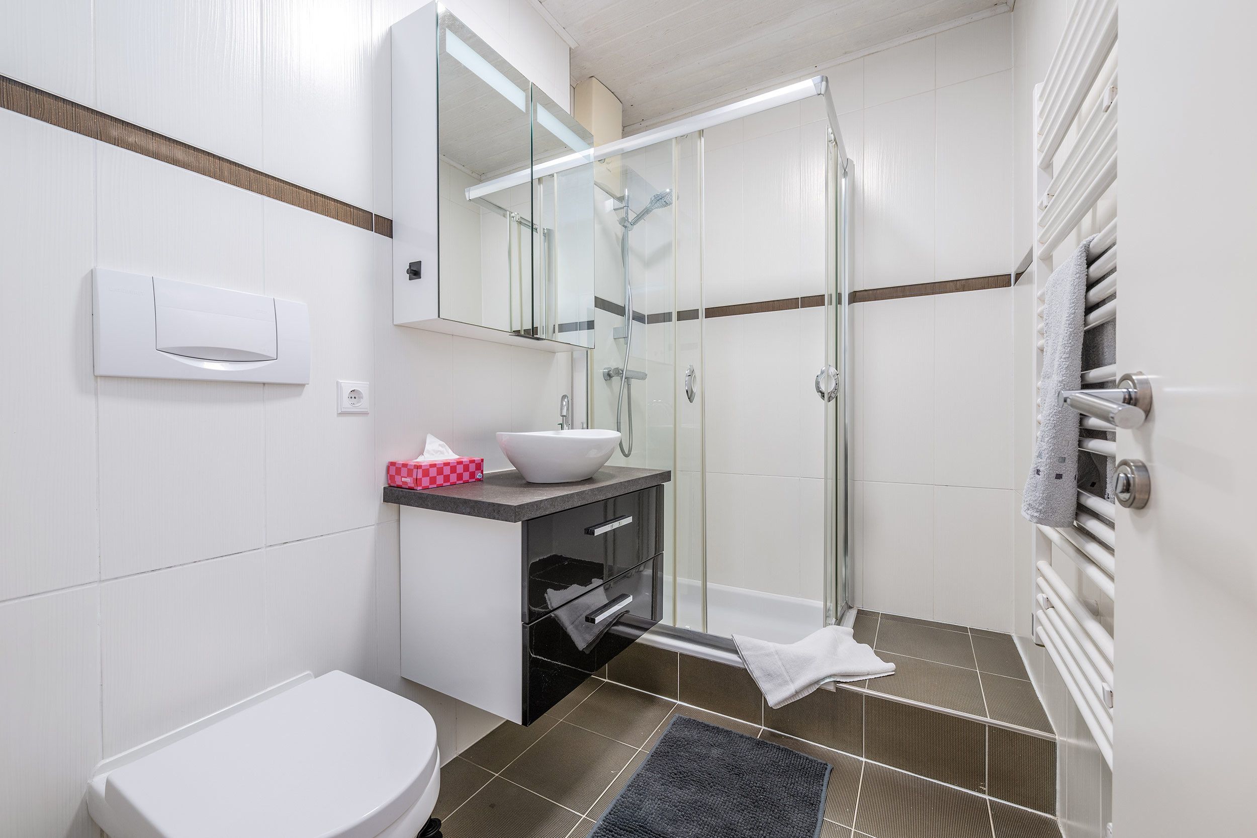 Ein modernes Badezimmer mit Toilette, Waschbecken, einer Duschkabine aus Glas und einem Handtuchhalter.
