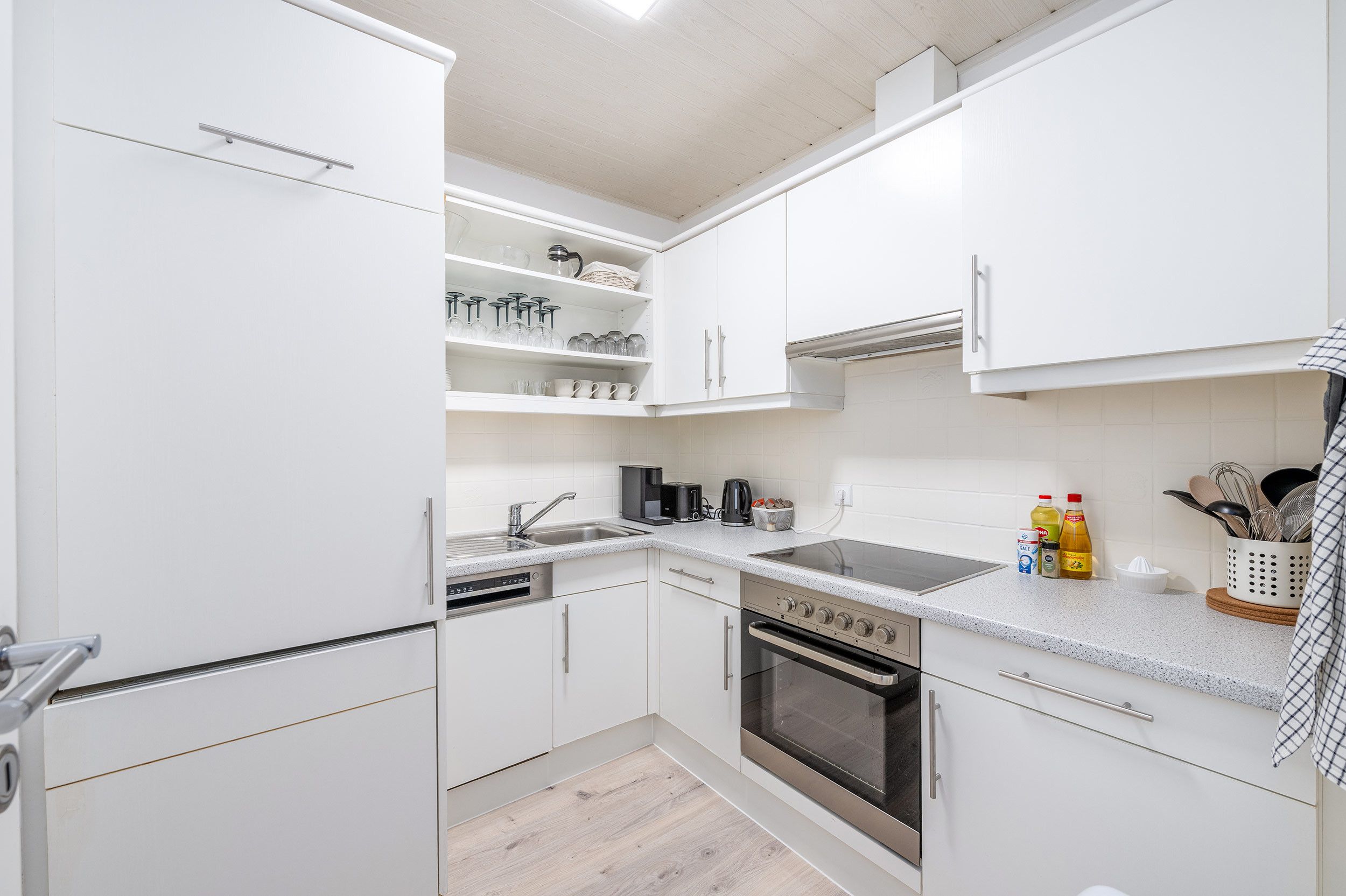 Een moderne keuken met witte kasten, een roestvrijstalen fornuis, een oven, een spoelbak en een aanrecht met diverse keukengerei.