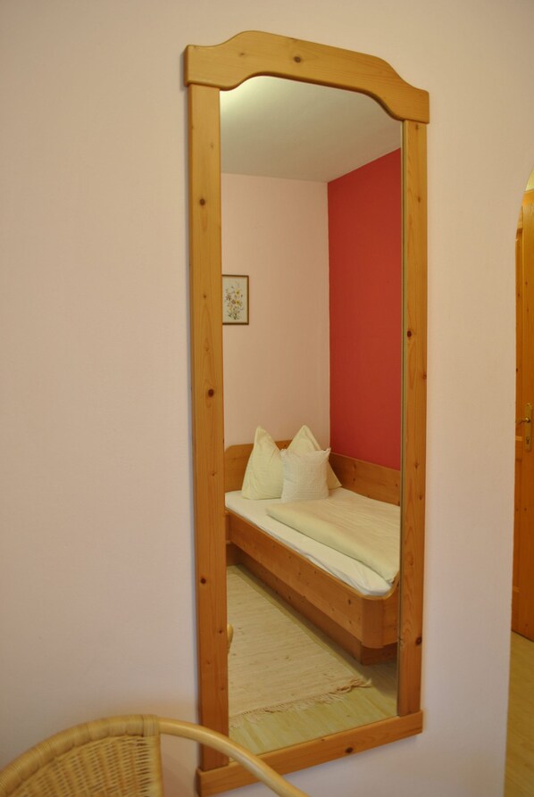 Una habitació amb un llit de fusta, un mirall i una cadira de vimet.