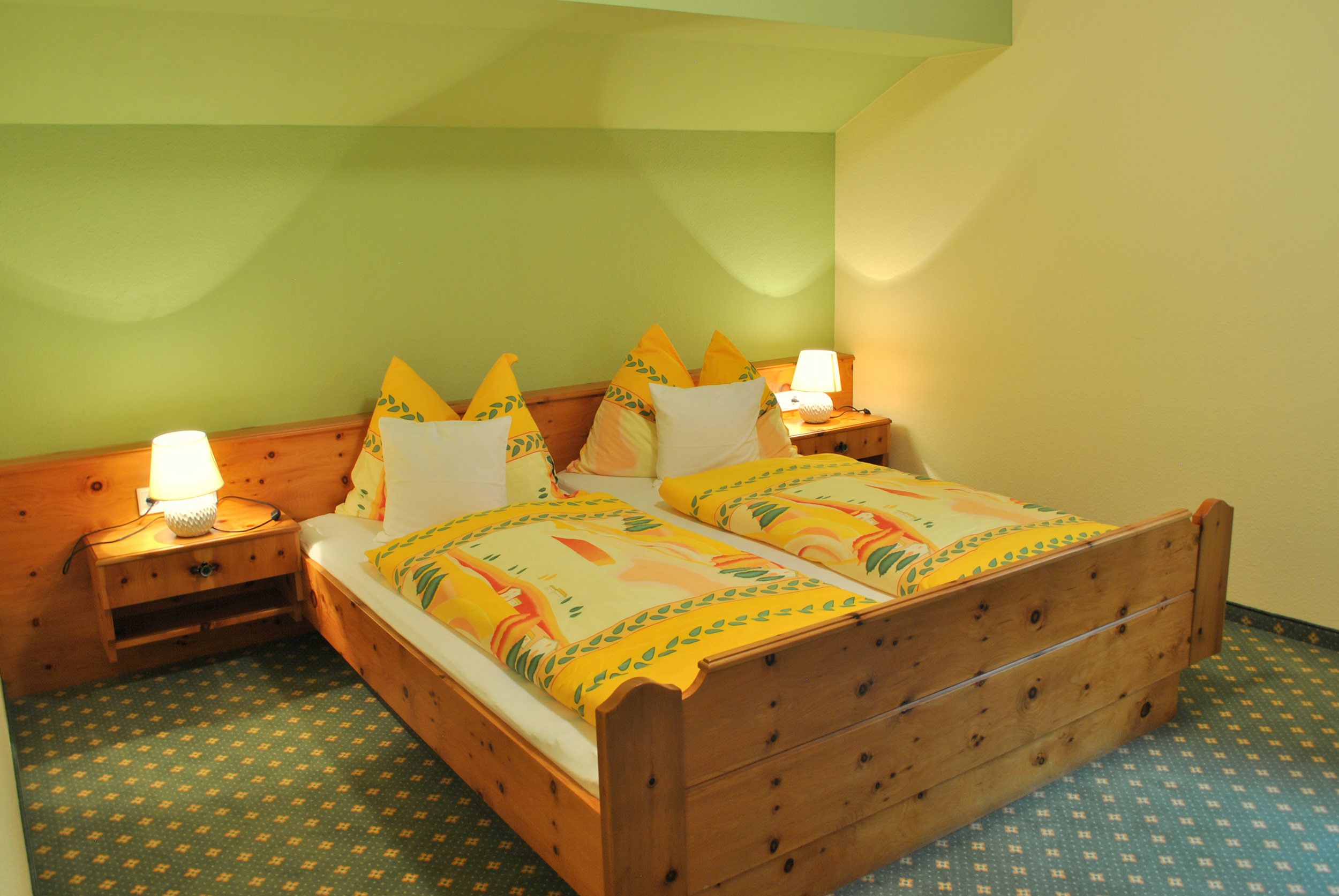 Ein Doppelbett mit Holzrahmen, zwei Nachttische inklusive Lampen und eine gemusterte Bettdecke.