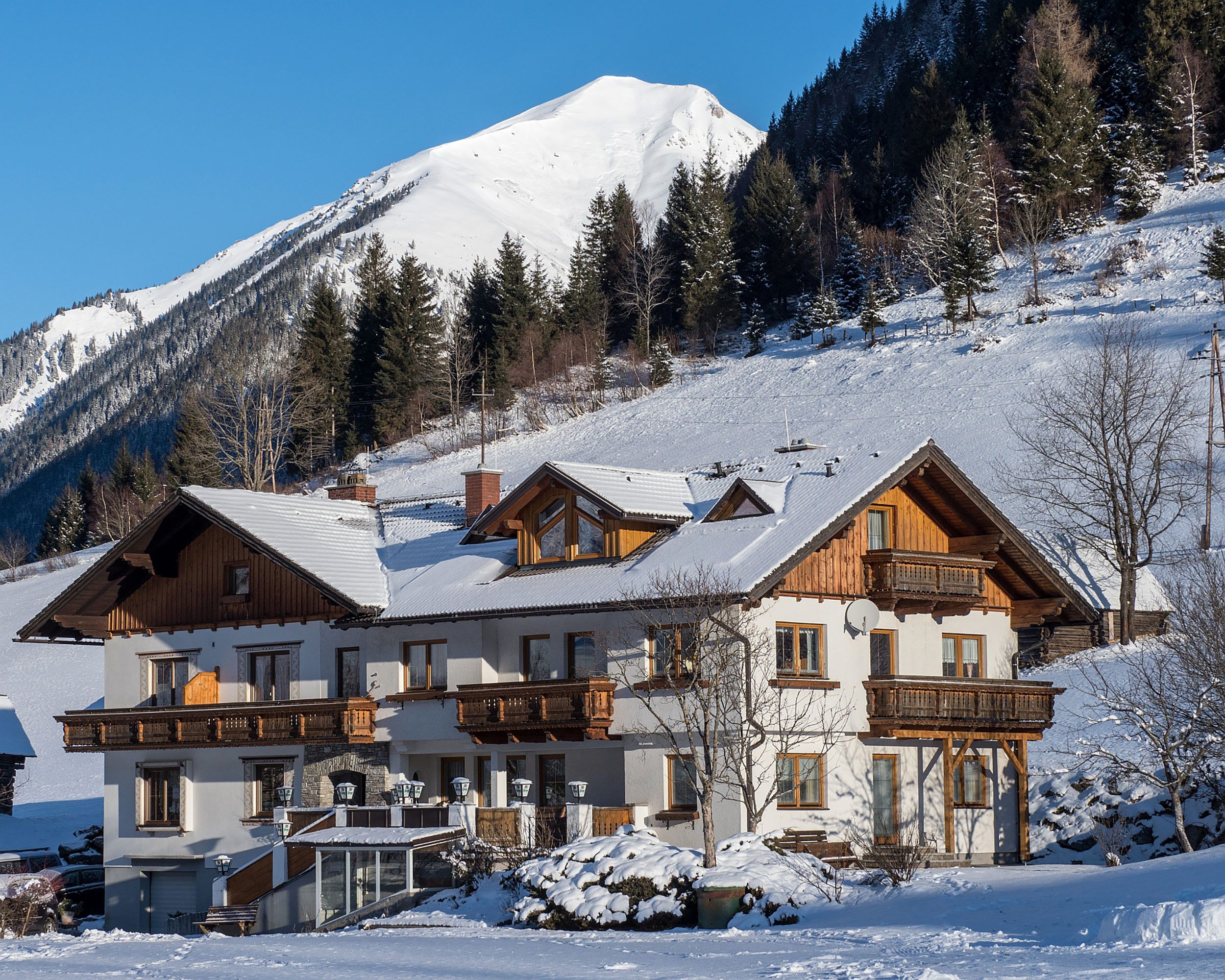 Un hotel de estilo chalet con techo nevado, balcones de madera y un paisaje de montañas al fondo.