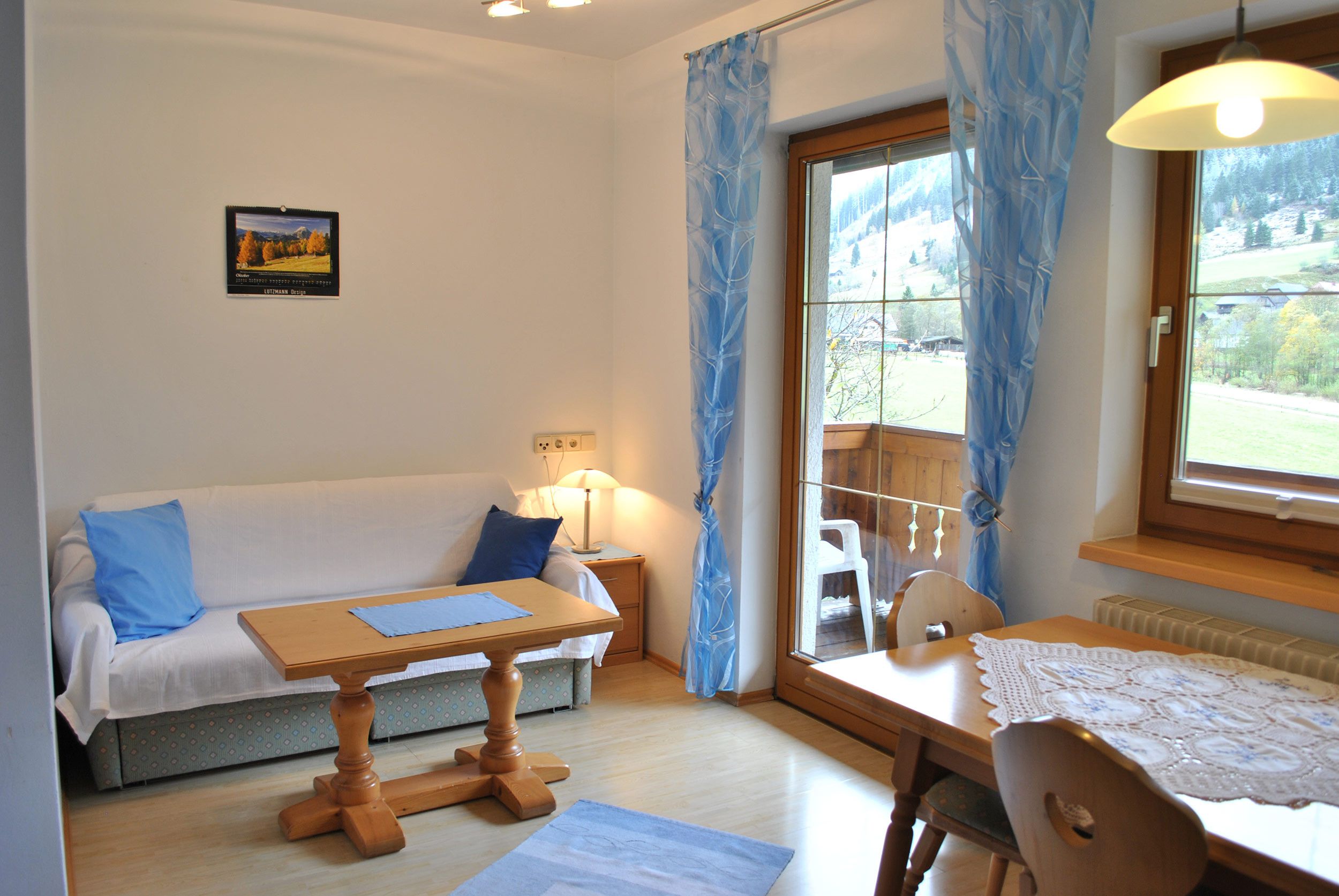 Una habitación acogedora con una mesa de madera, un sofá con cojines azules, una ventana con cortinas y una lámpara en una mesita de noche.