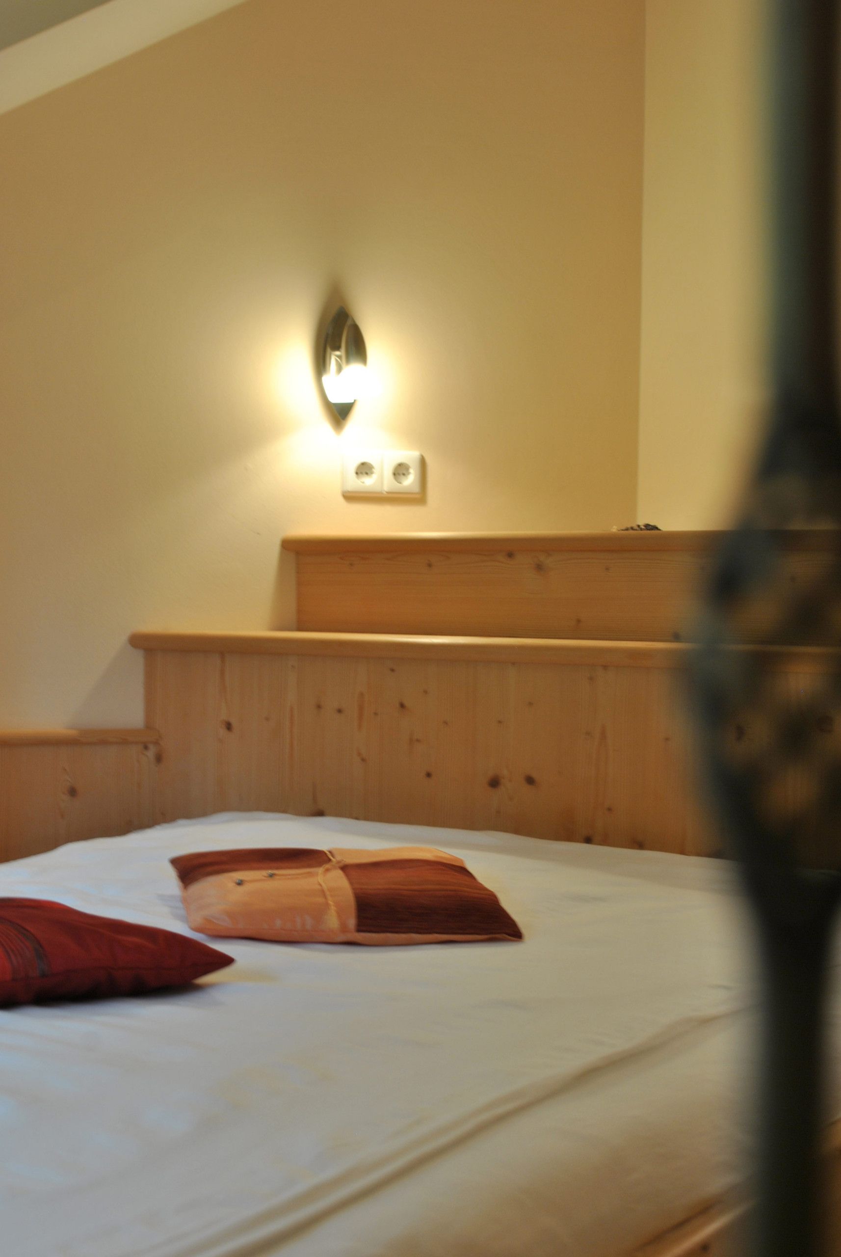 A bedroom with a wooden headboard, a bed with white bedding, and a wall-mounted light fixture.