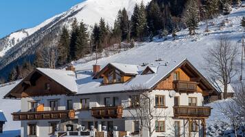 Un hotel de estilo chalet con techo nevado, balcones de madera y un paisaje de montañas al fondo.