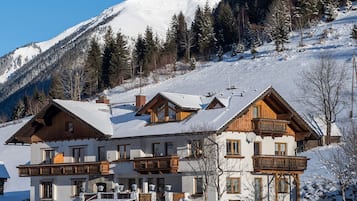 Un hotel de estilo chalet con techo nevado, balcones de madera y un paisaje de montañas al fondo.
