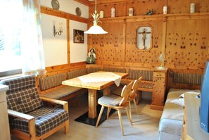 Une pièce chaleureuse avec un banc en bois servant de coin salon, une table et une croix accrochée au mur.