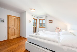 Een slaapkamer met een houten deur, een raam met gordijnen, een bed met witte lakens en een radiator.