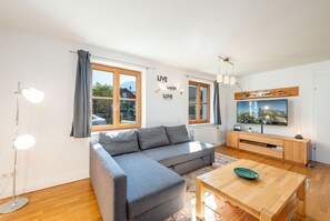 Uma sala de estar moderna com um sofá cinza, mesa de centro de madeira e uma TV na parede.
