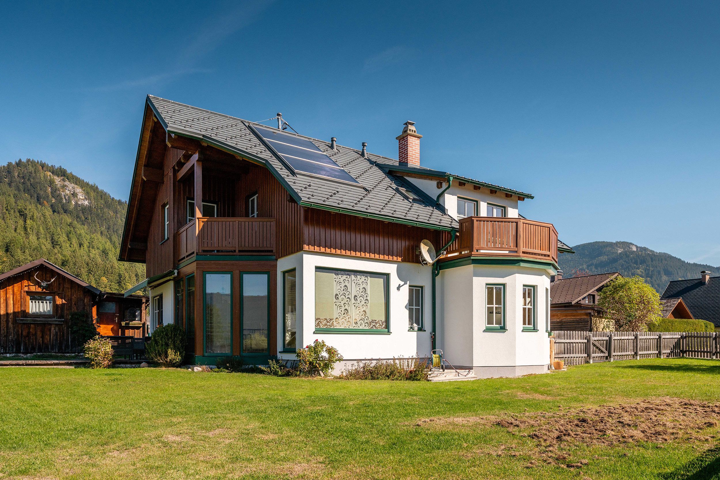 Uma casa de madeira de dois andares com telhado inclinado, painéis solares e uma grande janela com vidro decorativo.