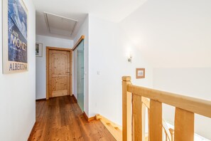 Corredor com piso de madeira, porta de madeira e porta de vidro que dá para um banheiro.