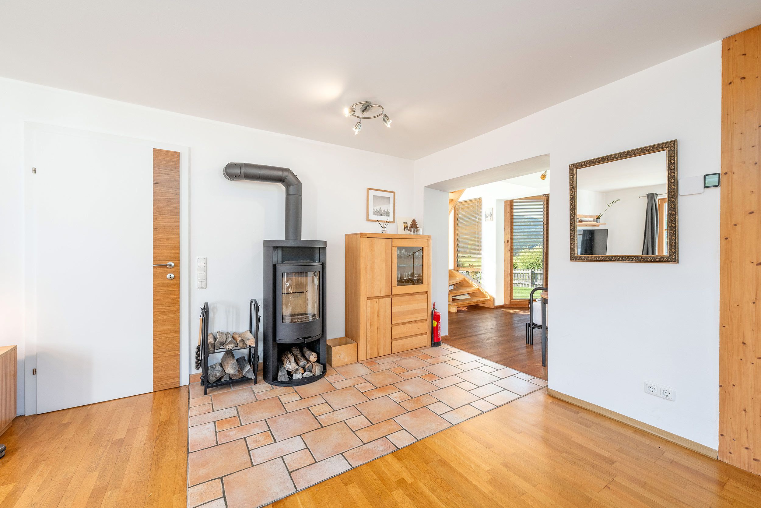 Ein modernes Interieur mit Kaminofen, Holzschrank und Spiegel an der Wand.