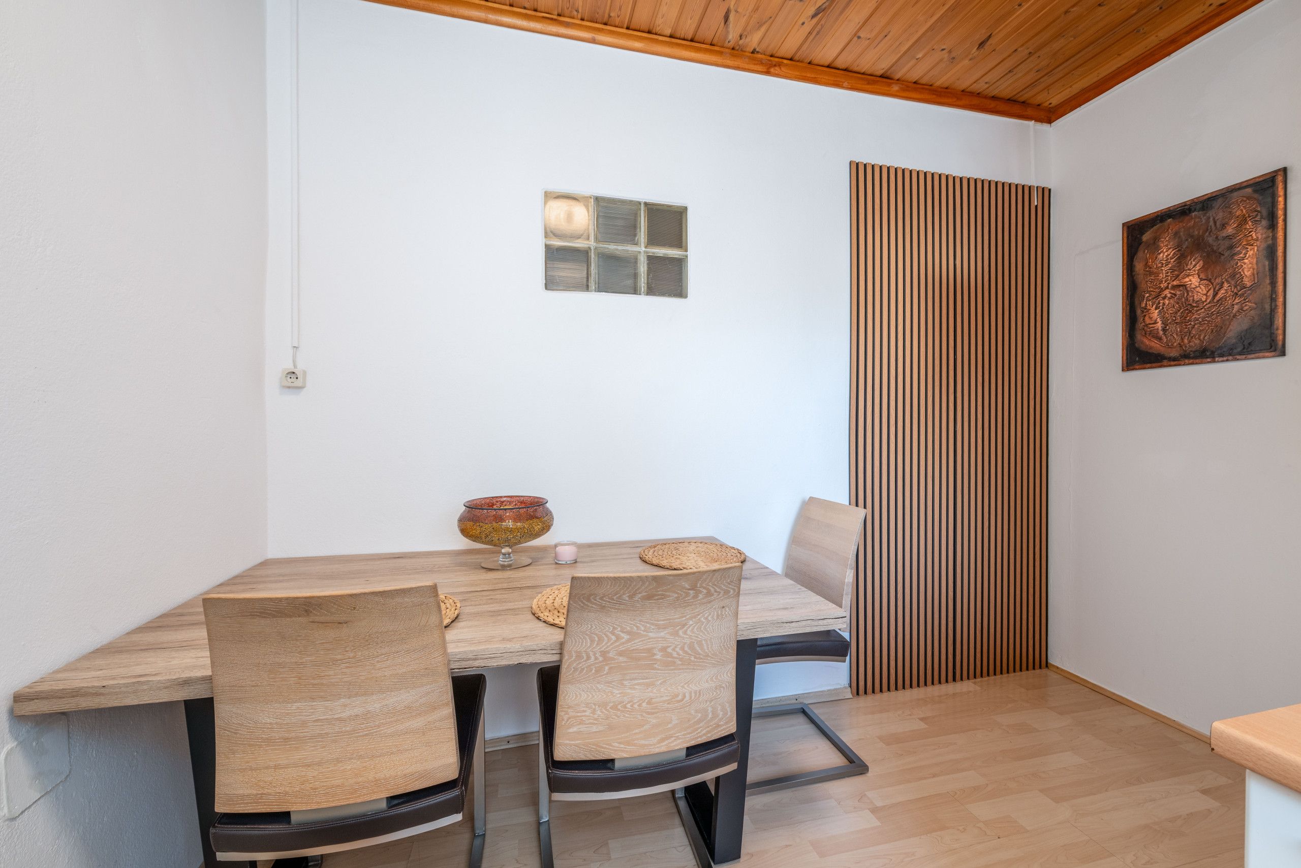 Un'area pranzo con un tavolo e sedie in legno, una piccola ciotola decorativa e un lampadario a parete.