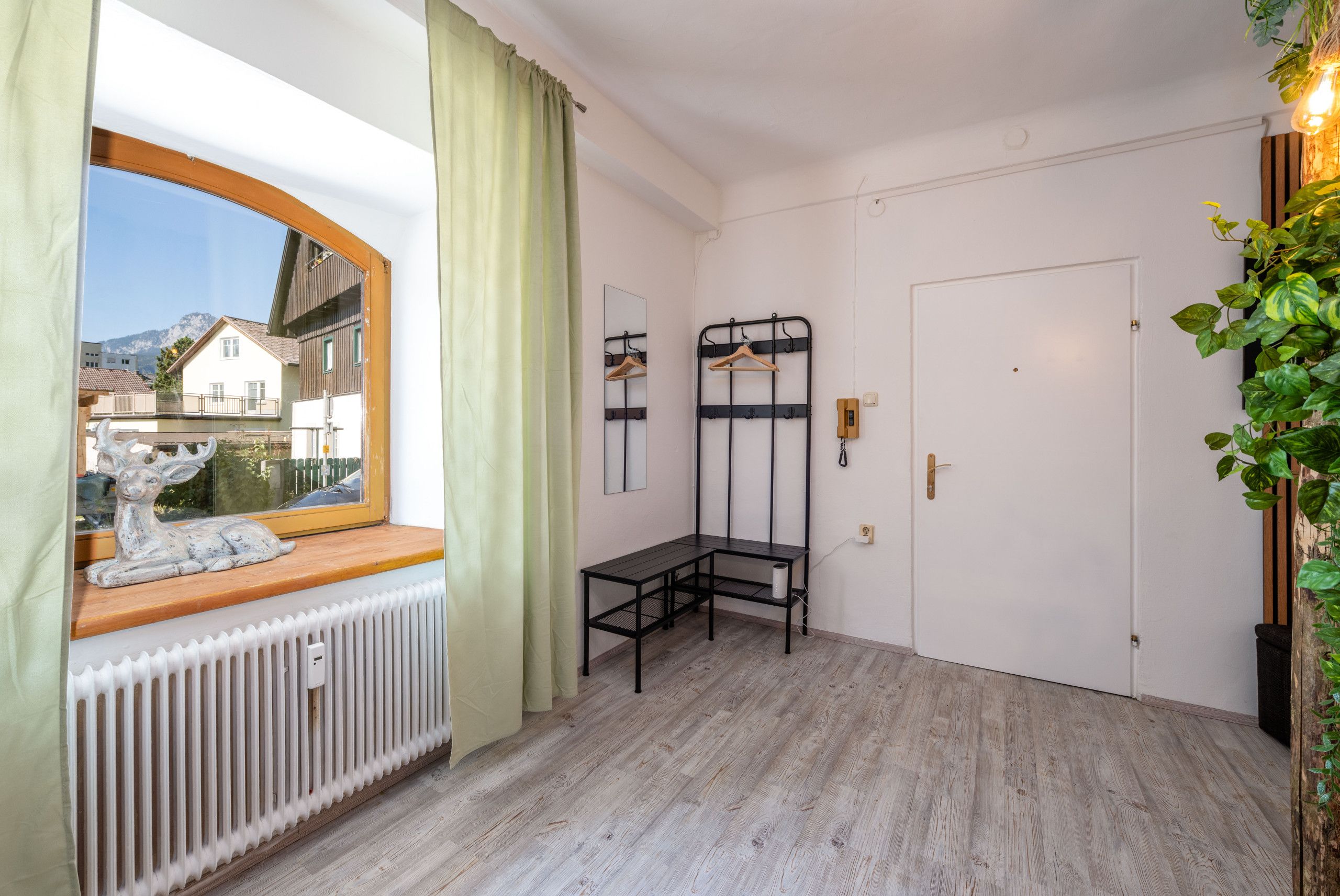 Una stanza con finestra, termosifone, panchina in legno, appendiabiti e una porta.