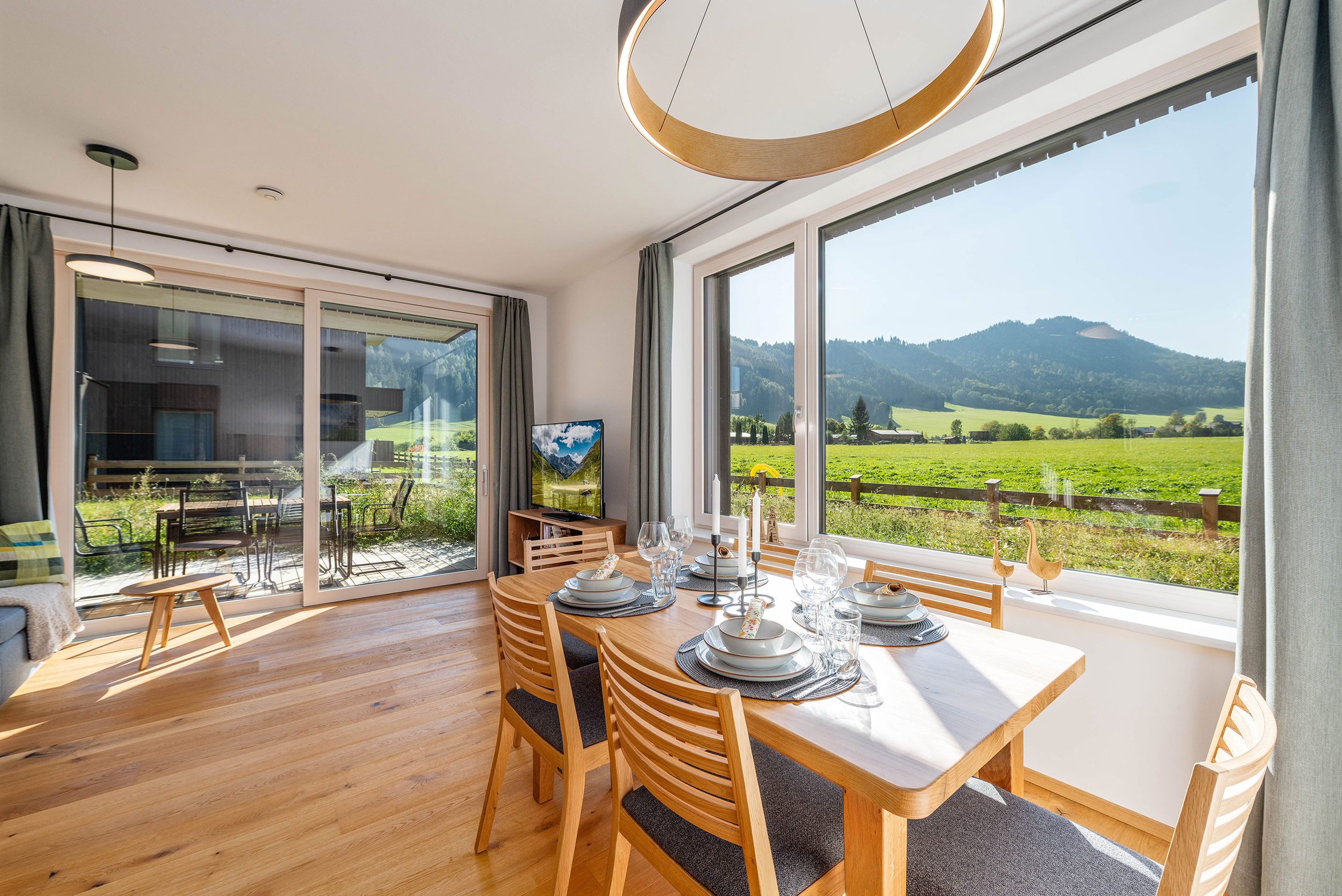 Een eetruimte met een tafel gedekt voor vier personen, grote ramen met uitzicht op een groen landschap en bergen, en een modern interieur.