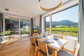 A dining area with a table set for four, large windows offering a view of a green landscape and mountains, and a modern interior design. - Mountain Paradise - Kamm 1 (Gröbming)