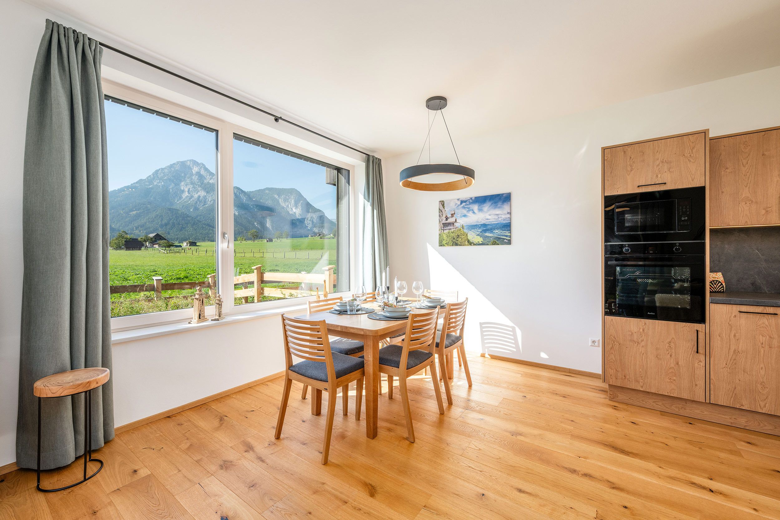 A modern kitchen with wooden cabinets, a dining table set for four, and a large window offering a mountain view.