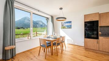 A modern kitchen with wooden cabinets, a dining table set for four, and a large window offering a mountain view.