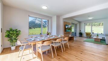 A spacious dining area with a long wooden table, multiple chairs, and a view of a mountainous landscape through large windows.