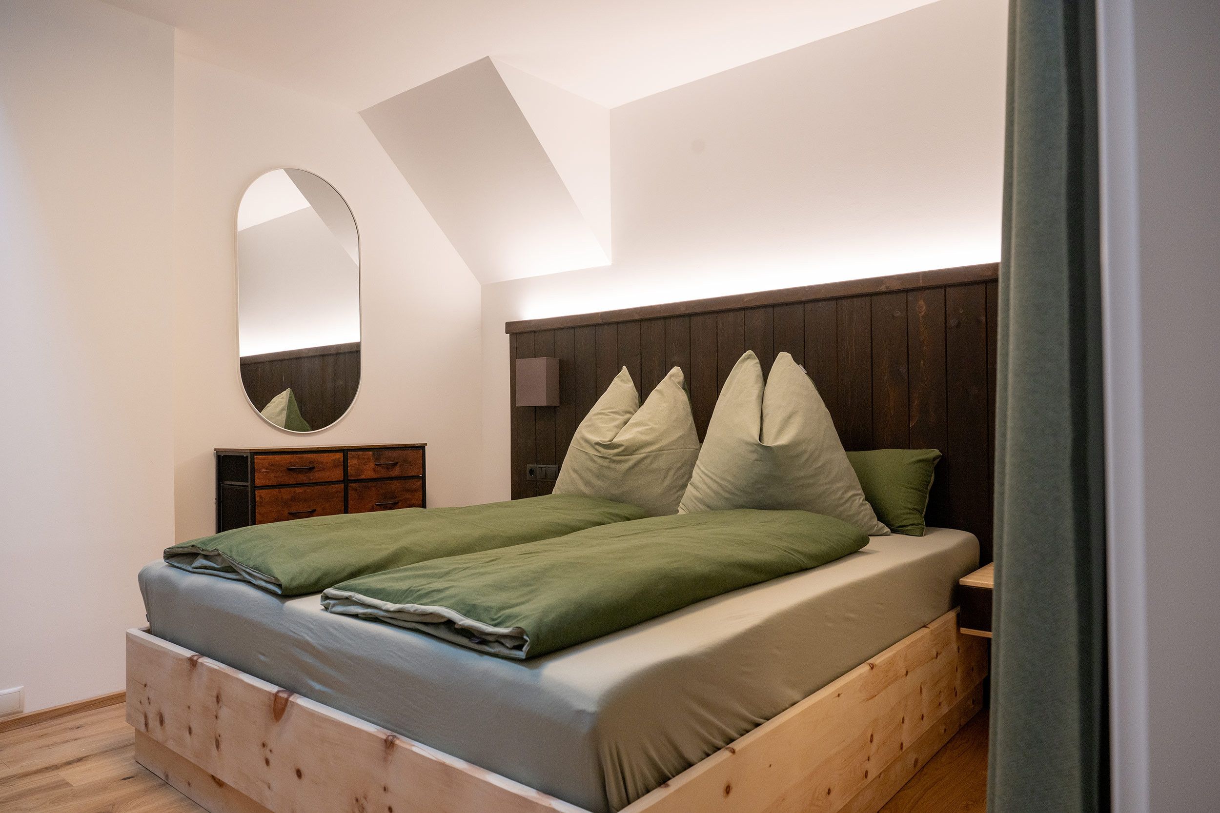 Une chambre à coucher avec un lit en bois, une table de chevet, un miroir et un plafond en pente.