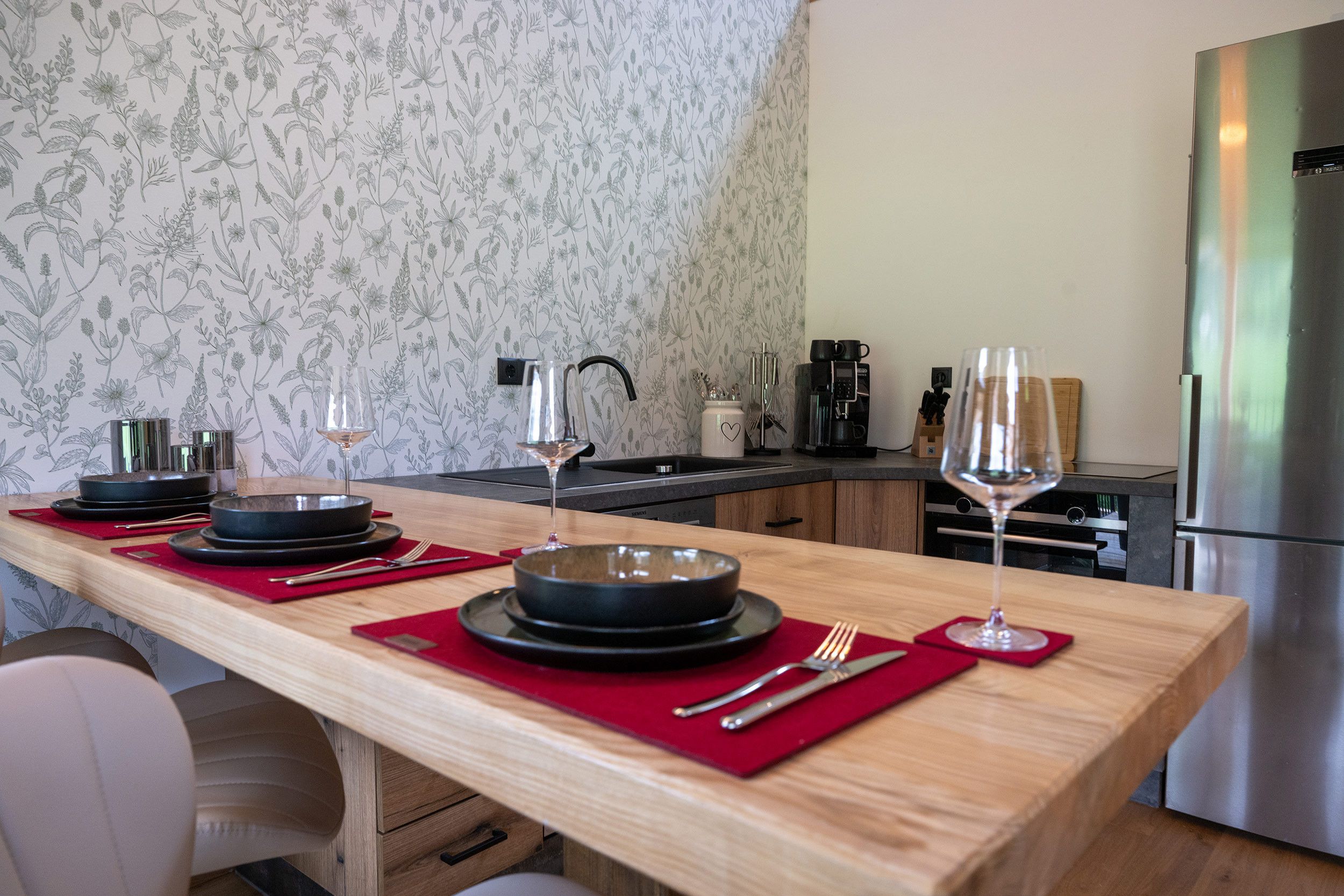 Une cuisine avec une table en bois mise pour le repas, équipée d’assiettes, de couverts et de verres.