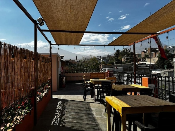 An outdoor patio area with tables and chairs, a wooden fence, and a view of a mountain in the background. - Olespier Hostel (AREQUIPA)