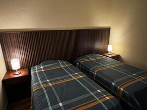A hotel room with two beds, each with a plaid bedspread, a wooden headboard, and bedside lamps. - Olespier Hostel (AREQUIPA)