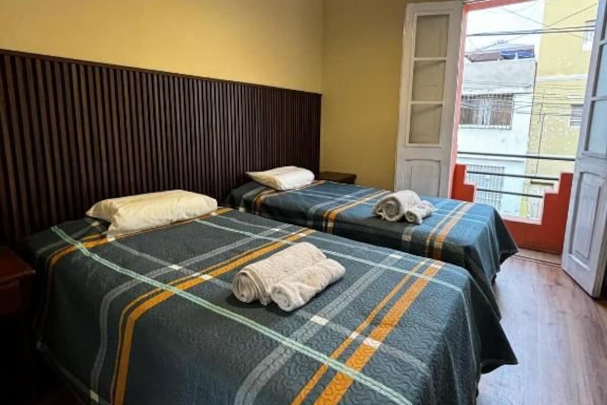 A hotel room with two beds, a wooden headboard, a window with a view, and a door.