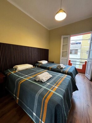 A hotel room with two beds, a wooden headboard, a window with a view, and a door. - Olespier Hostel (AREQUIPA)