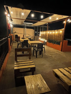 An outdoor patio area with wooden tables and benches, string lights, and a covered section. - Olespier Hostel (AREQUIPA)