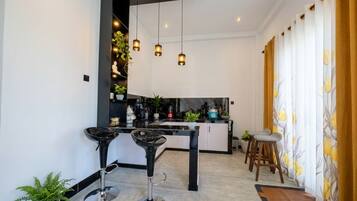 Una cocina moderna con una isla central, taburetes de bar, lámparas colgantes y vistas al área de estar contigua.
