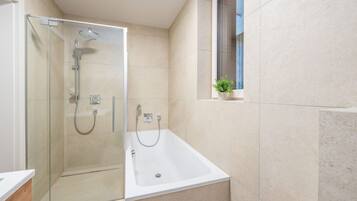 Ein modernes Badezimmer mit Duschkabine aus Glas, einer Badewanne und einem kleinen Fenster mit Pflanze.
