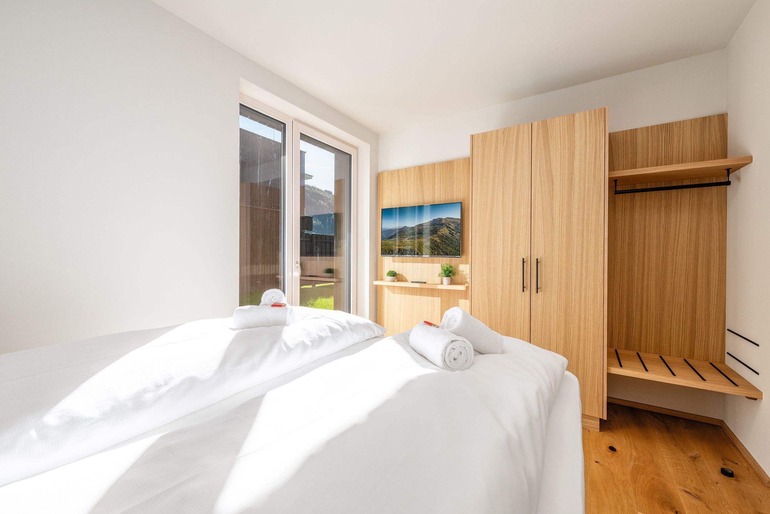 Een moderne slaapkamer met een groot bed, een houten garderobe en een raam met uitzicht op de bergen.