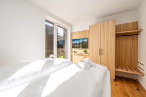 Een moderne slaapkamer met een groot bed, een houten garderobe en een raam met uitzicht op de bergen.