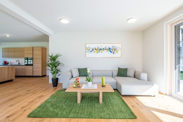 Een moderne woonkamer met een hoekbank, een salontafel, een kamerplant en een schilderij aan de muur.