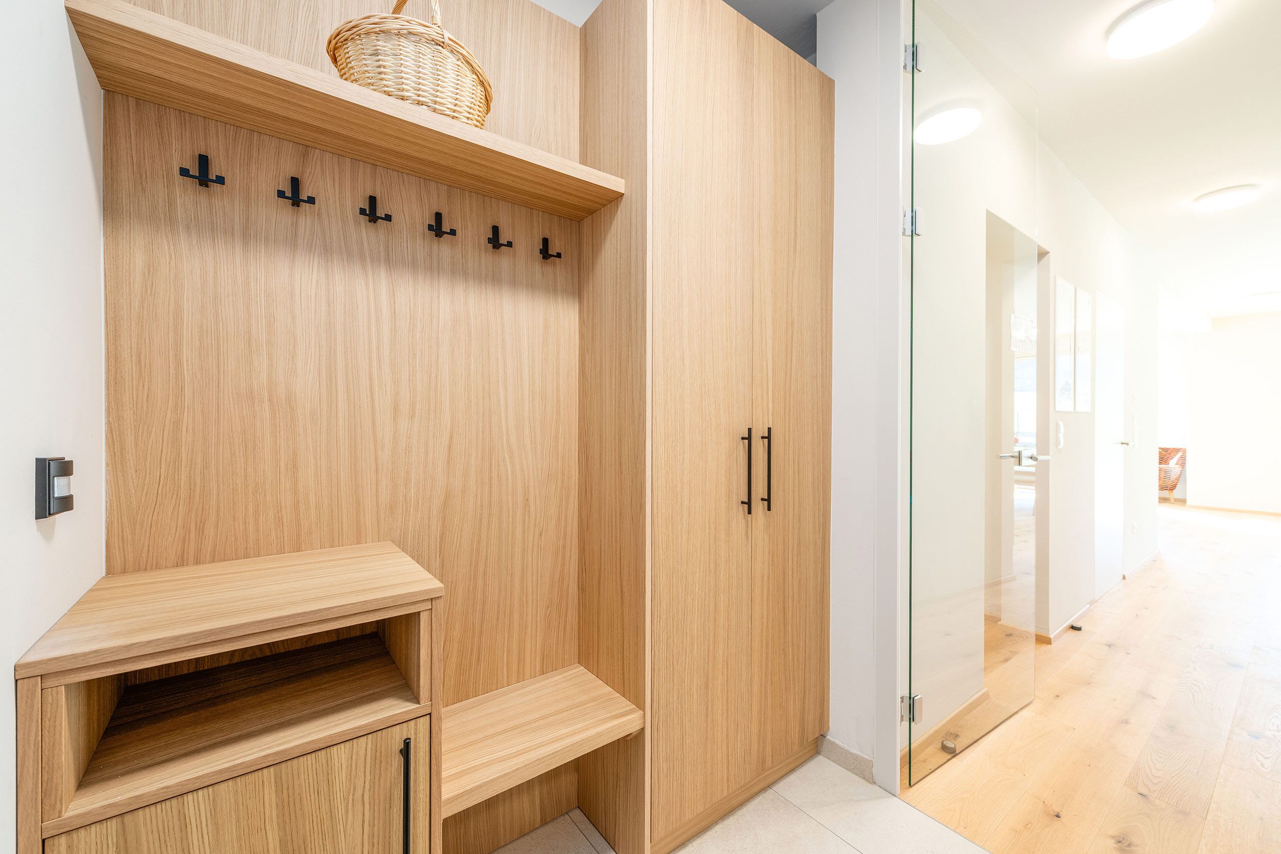 A modern interior with a wooden wardrobe, a glass door, and a built-in bench.