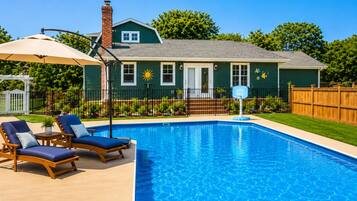 A swimming pool with lounge chairs and a house in the background.