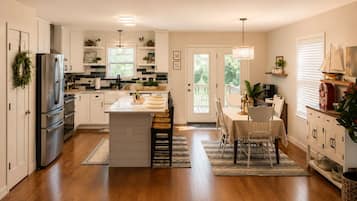 A kitchen with white cabinets, a refrigerator, a dining area with a table and chairs, and a window with blinds.