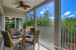 Un espace extérieur abrité, aménagé pour les repas, avec des chaises en osier et une table en verre, donnant sur un jardin.